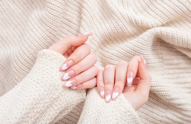 female hands with beautiful long nails with  manicure with  heart pattern in winter clothes